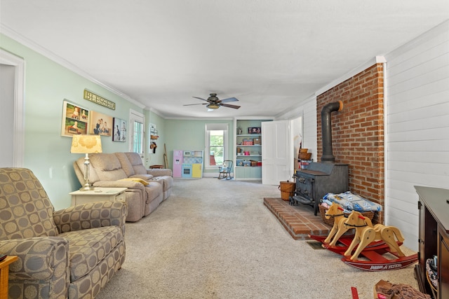 carpeted living room featuring ornamental molding, a wood stove, and ceiling fan