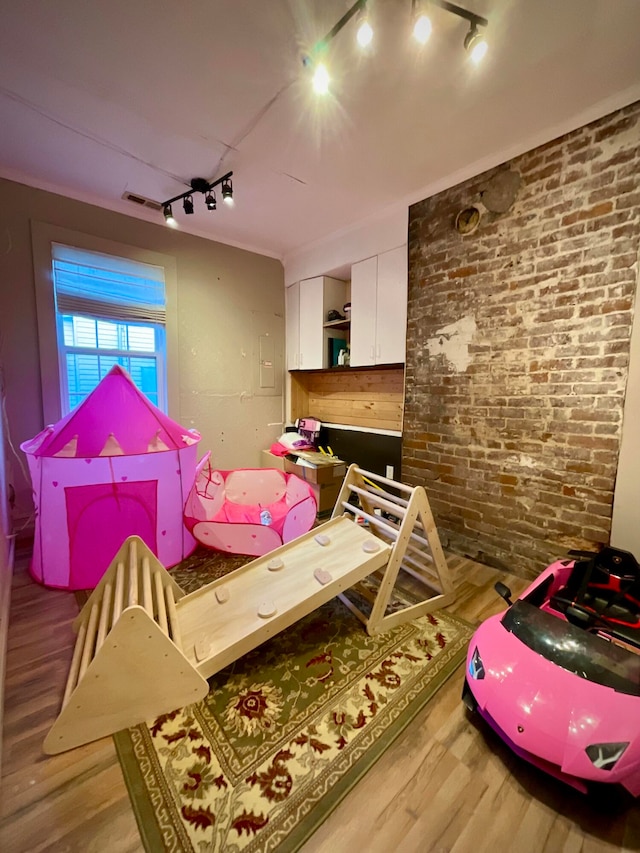 game room featuring brick wall, track lighting, and hardwood / wood-style flooring