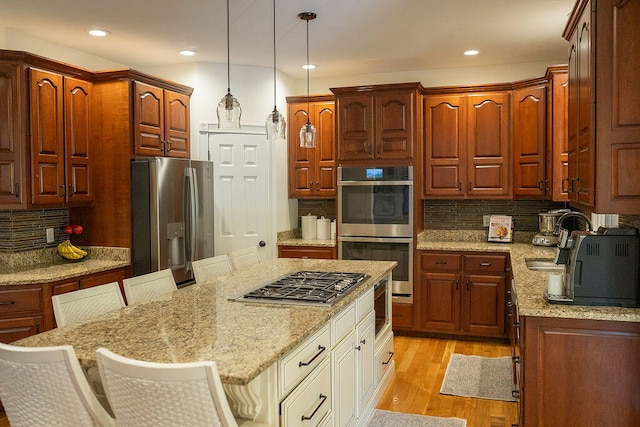 kitchen featuring light stone counters, backsplash, pendant lighting, stainless steel appliances, and light hardwood / wood-style flooring