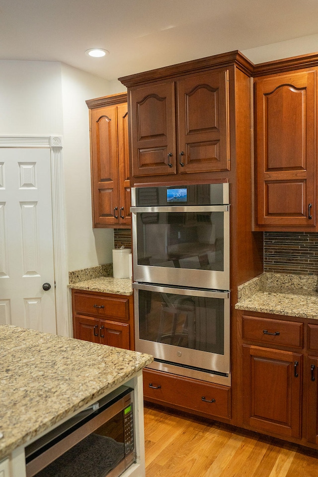 kitchen with decorative backsplash, stainless steel appliances, light stone counters, and light hardwood / wood-style floors