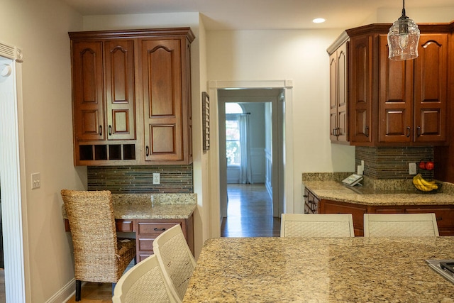 kitchen featuring dark wood-type flooring, light stone counters, decorative light fixtures, and tasteful backsplash