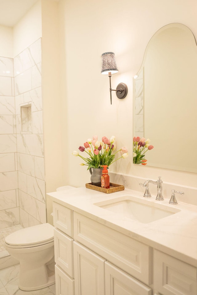 bathroom with tiled shower, vanity, and toilet