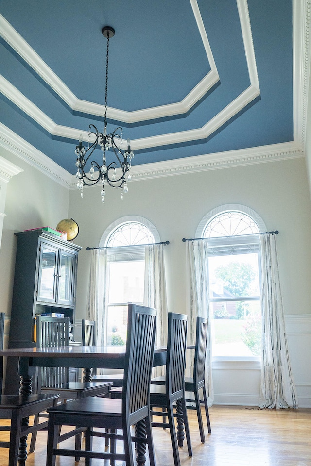 dining area featuring ornamental molding, a raised ceiling, a chandelier, and light hardwood / wood-style floors