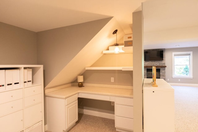 unfurnished office featuring built in desk, light colored carpet, and a stone fireplace