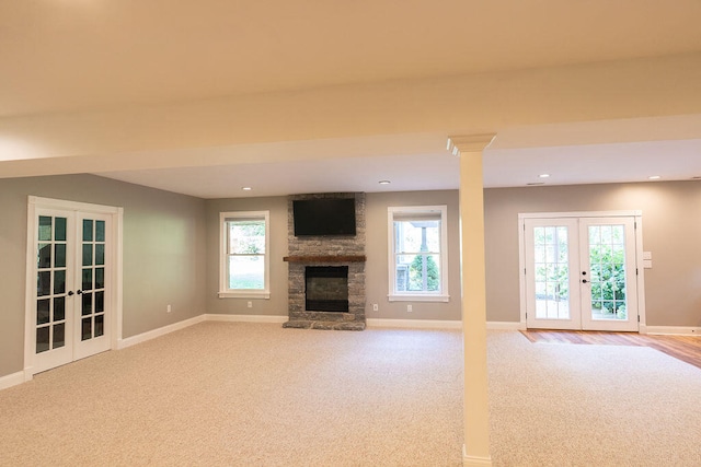 unfurnished living room with a healthy amount of sunlight, french doors, and a stone fireplace