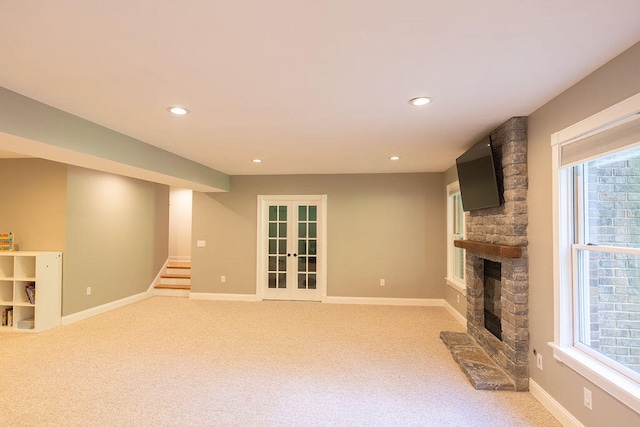 unfurnished living room with a stone fireplace, carpet flooring, and french doors