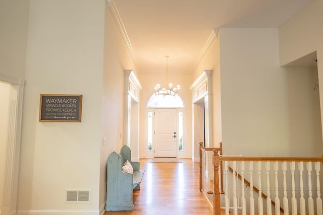 foyer entrance with crown molding, light hardwood / wood-style floors, and a chandelier