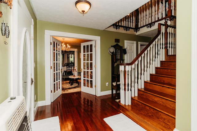 entrance foyer featuring heating unit, dark wood-type flooring, a textured ceiling, an inviting chandelier, and french doors