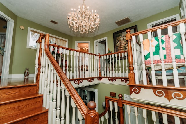 stairs with a textured ceiling and a notable chandelier