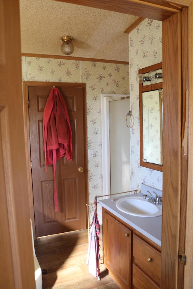 bathroom with a textured ceiling, crown molding, vanity, and hardwood / wood-style flooring