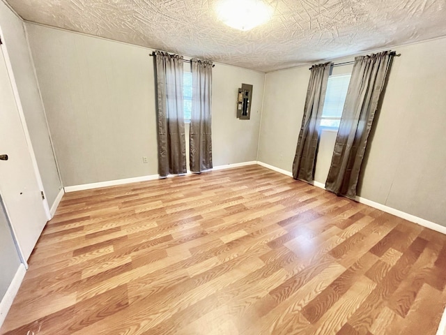 unfurnished room featuring light wood-type flooring, a textured ceiling, and electric panel