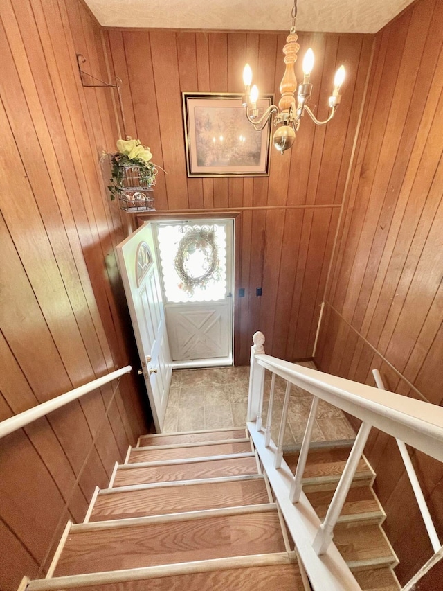 stairway with an inviting chandelier, wooden walls, and tile patterned flooring