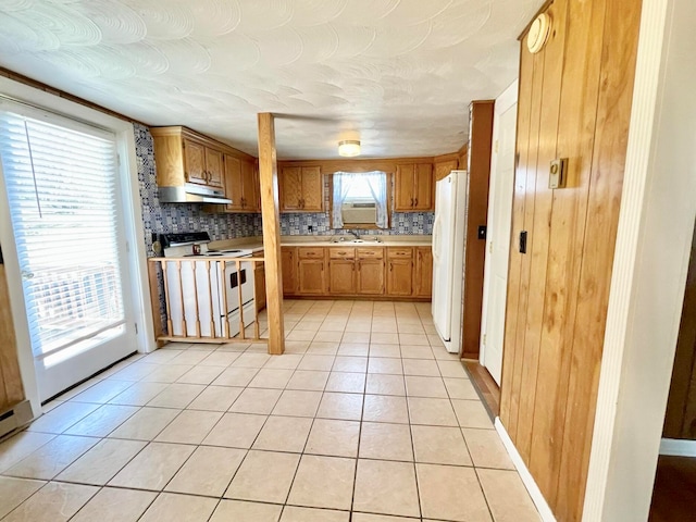 kitchen with a wealth of natural light, white appliances, light tile patterned floors, and backsplash