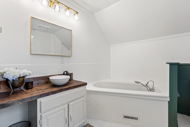 bathroom featuring a bathtub, lofted ceiling, a textured ceiling, and vanity