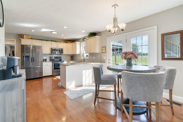 kitchen featuring appliances with stainless steel finishes, hanging light fixtures, light stone counters, tasteful backsplash, and light hardwood / wood-style flooring