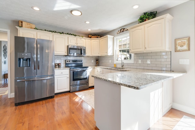 kitchen featuring light hardwood / wood-style floors, sink, kitchen peninsula, stainless steel appliances, and light stone countertops