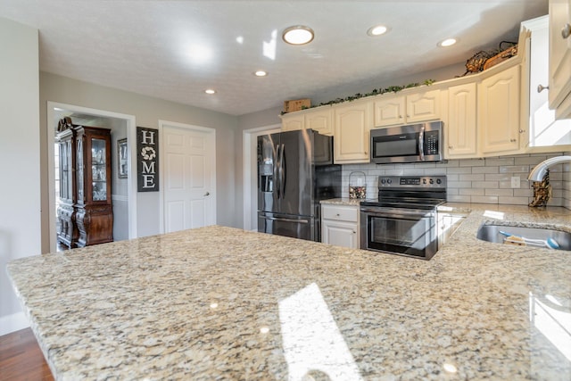 kitchen featuring light stone counters, sink, tasteful backsplash, appliances with stainless steel finishes, and hardwood / wood-style floors