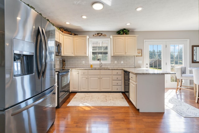 kitchen with hardwood / wood-style flooring, kitchen peninsula, decorative backsplash, appliances with stainless steel finishes, and light stone countertops