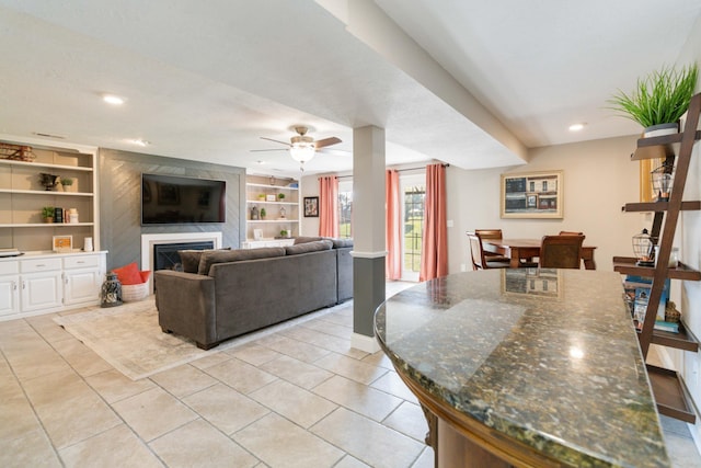 tiled living room with built in shelves, a large fireplace, and ceiling fan