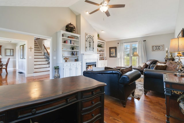 living room featuring high vaulted ceiling, wood-type flooring, a tiled fireplace, and ceiling fan