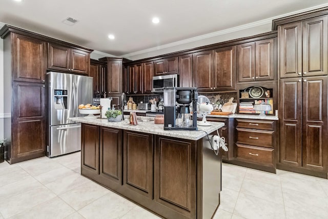 kitchen featuring tasteful backsplash, stainless steel appliances, crown molding, dark brown cabinetry, and a kitchen island with sink