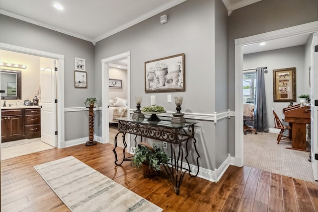 corridor with light wood-type flooring, crown molding, and sink