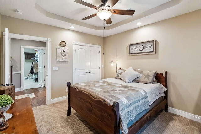 bedroom with ceiling fan, a closet, hardwood / wood-style floors, and a tray ceiling