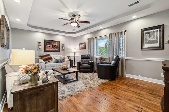 living room with light hardwood / wood-style flooring, ceiling fan, and a raised ceiling