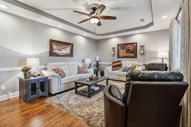 living room with wood-type flooring, ceiling fan, and a raised ceiling