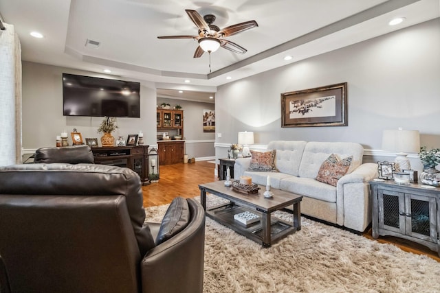 living room with wood-type flooring, ceiling fan, and a raised ceiling