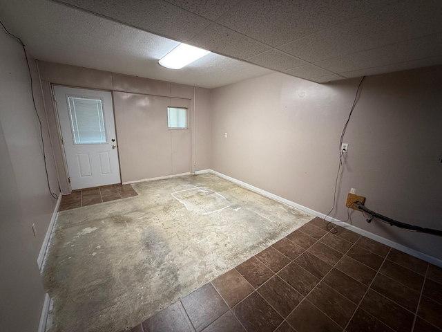 basement with a paneled ceiling and baseboards