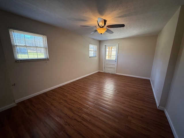 empty room featuring dark wood-type flooring, ceiling fan, a textured ceiling, and baseboards