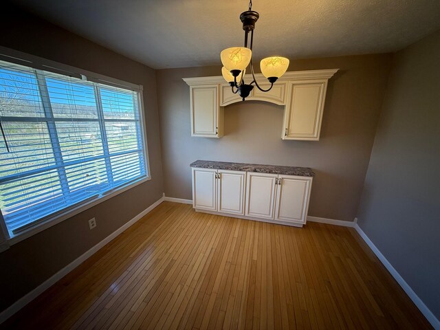 unfurnished room featuring a chandelier, light wood finished floors, a textured ceiling, and baseboards