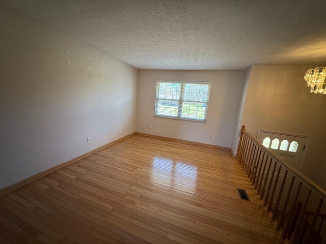 spare room with a textured ceiling, a notable chandelier, visible vents, baseboards, and light wood-type flooring