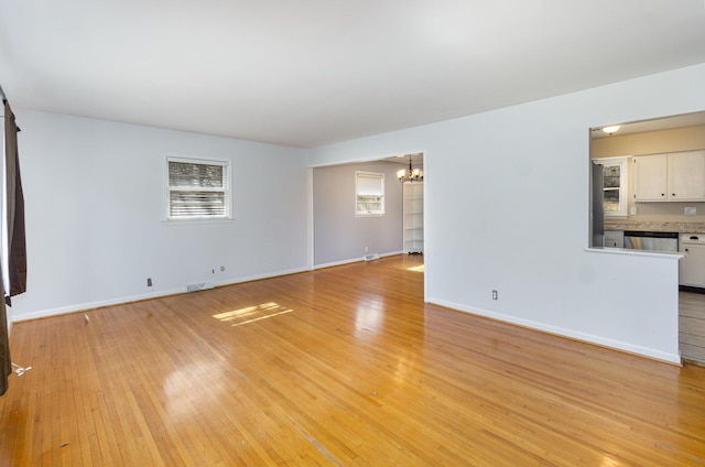 unfurnished living room with light wood-style flooring, visible vents, baseboards, and a notable chandelier