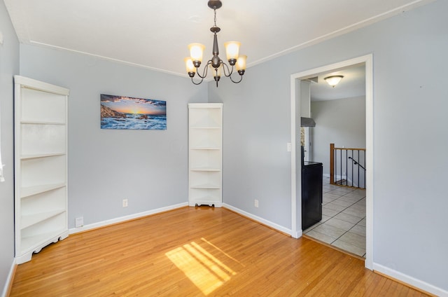 empty room featuring a chandelier, light wood-type flooring, and baseboards