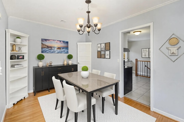 dining area with baseboards, light wood finished floors, crown molding, and an inviting chandelier