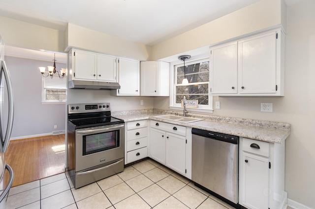 kitchen with light tile patterned floors, under cabinet range hood, stainless steel appliances, a sink, and white cabinetry