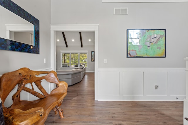 interior space featuring vaulted ceiling with beams, visible vents, a decorative wall, wainscoting, and wood finished floors