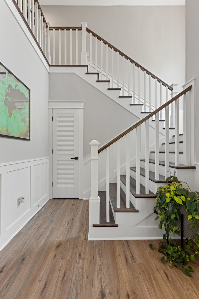 stairway with a wainscoted wall, a high ceiling, wood finished floors, and a decorative wall