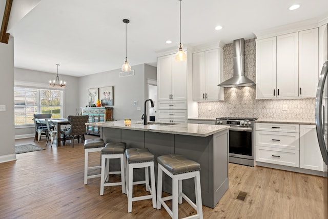 kitchen featuring a sink, visible vents, wall chimney range hood, backsplash, and stainless steel range with gas cooktop