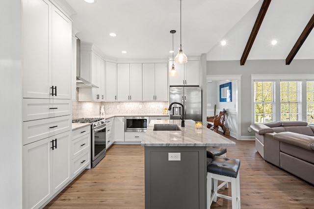 kitchen featuring open floor plan, a sink, stainless steel appliances, wall chimney range hood, and backsplash