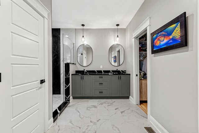 bathroom featuring a walk in closet, marble finish floor, double vanity, a sink, and baseboards