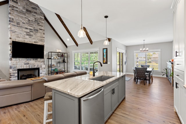 kitchen with light wood finished floors, dishwasher, gray cabinetry, a stone fireplace, and a sink