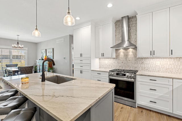 kitchen featuring stainless steel gas range oven, a sink, decorative backsplash, wall chimney exhaust hood, and light wood finished floors