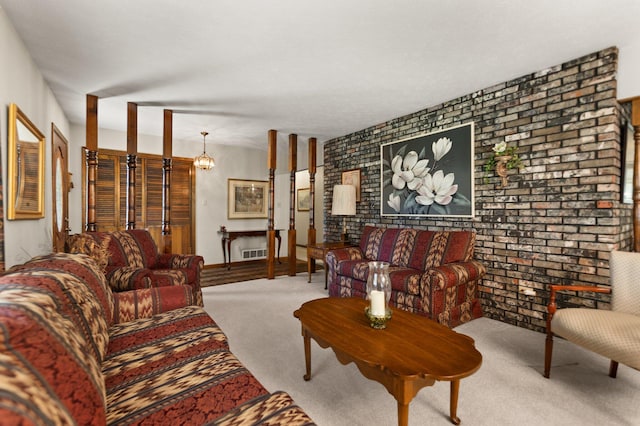 carpeted living room with a notable chandelier, a brick fireplace, and brick wall