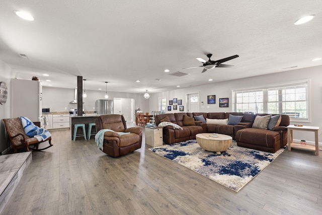 living room featuring ceiling fan, a textured ceiling, and light hardwood / wood-style flooring