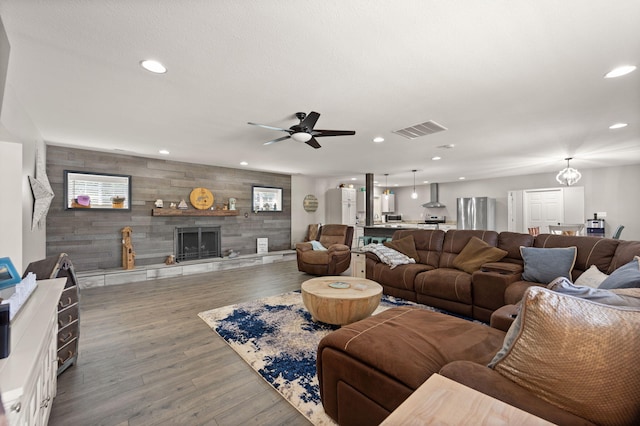 living room with wood-type flooring, wooden walls, ceiling fan, and a tile fireplace