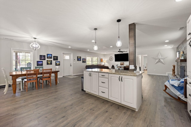 kitchen with white cabinets, light stone countertops, pendant lighting, dark hardwood / wood-style floors, and ceiling fan with notable chandelier