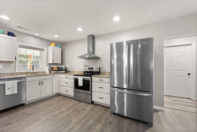 kitchen featuring white cabinets, appliances with stainless steel finishes, hardwood / wood-style flooring, and wall chimney range hood